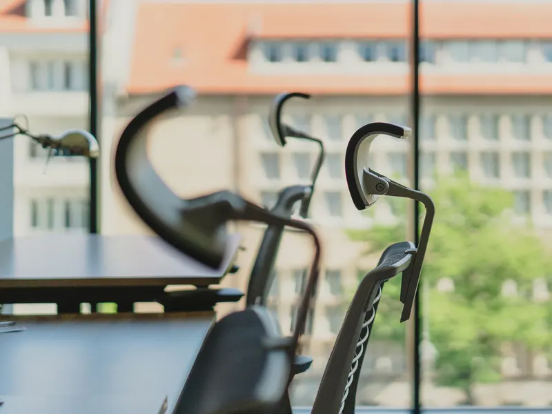 An orderly office with clear desks and modern chairs beside sunlit windows
